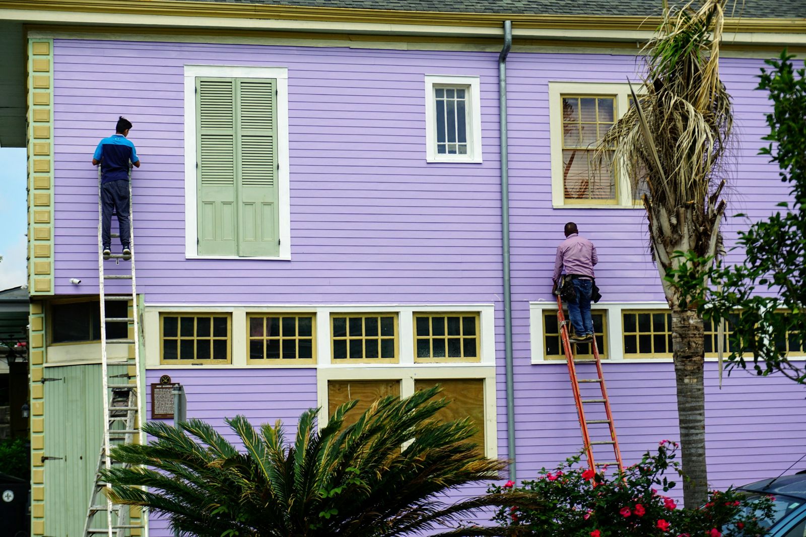 Two painters on ladders working on a house exterior
