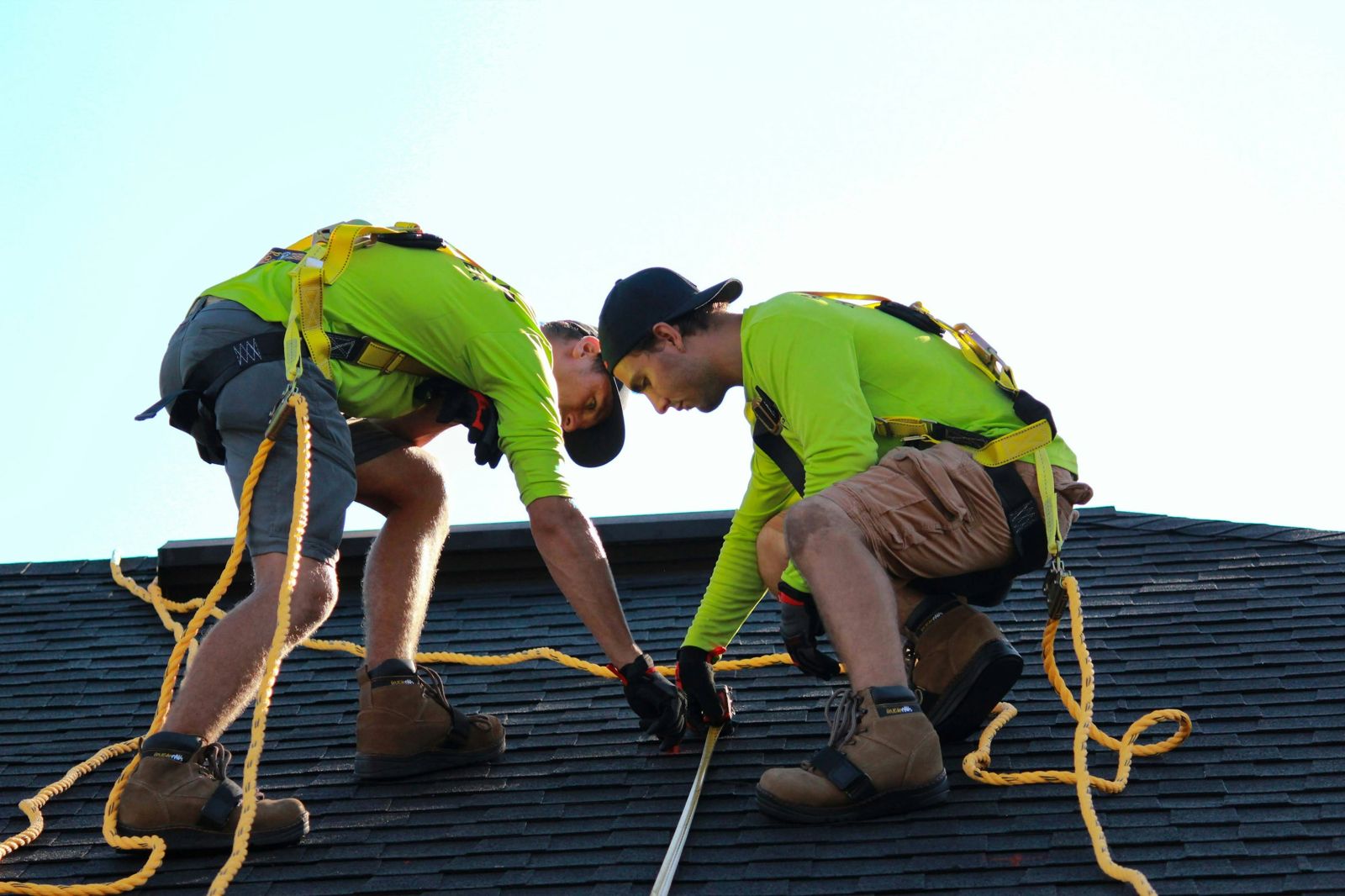 Two roofers in safety harnesses working on a shingle roof